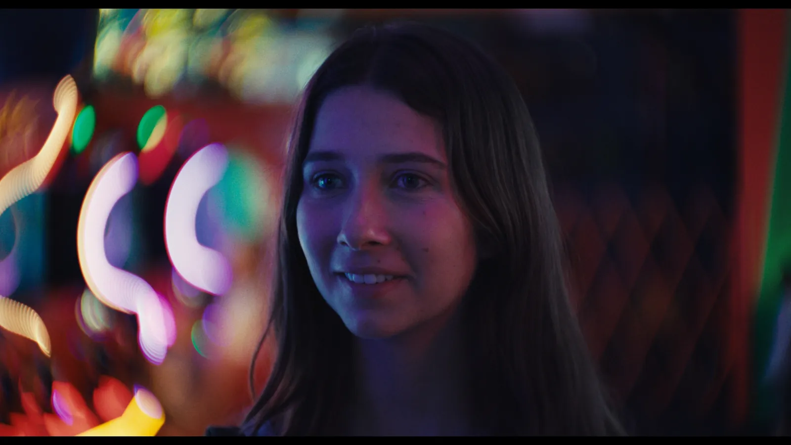 Perfect Love still — a young woman smiling amid glowing neon lights